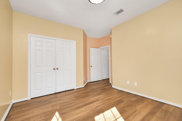 unfurnished bedroom featuring wood finished floors, a closet, baseboards, and visible vents
