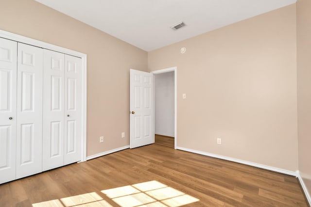unfurnished bedroom featuring wood finished floors, a closet, baseboards, and visible vents