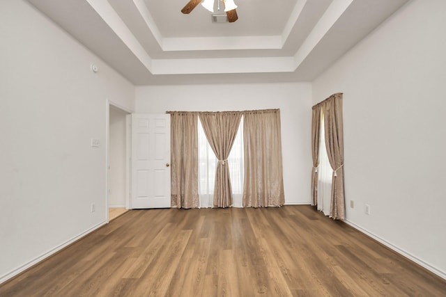 unfurnished room featuring a ceiling fan, a raised ceiling, wood finished floors, baseboards, and visible vents