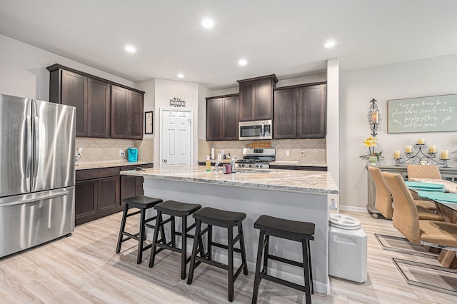 408 Long Beach Bay Dr, Katy, TX 77493 - kitchen featuring appliances with stainless steel finishes, dark brown cabinetry, a kitchen breakfast bar, light stone counters, and recessed lighting
