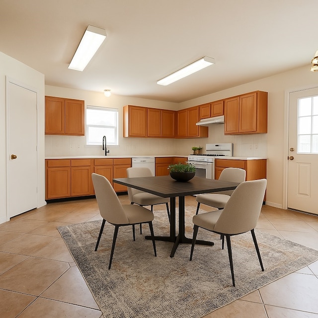 kitchen with under cabinet range hood, light tile patterned floors, white appliances, a sink, and light countertops