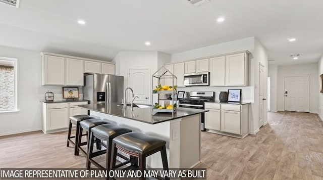 kitchen with a breakfast bar area, a sink, dark countertops, stainless steel appliances, and light wood finished floors