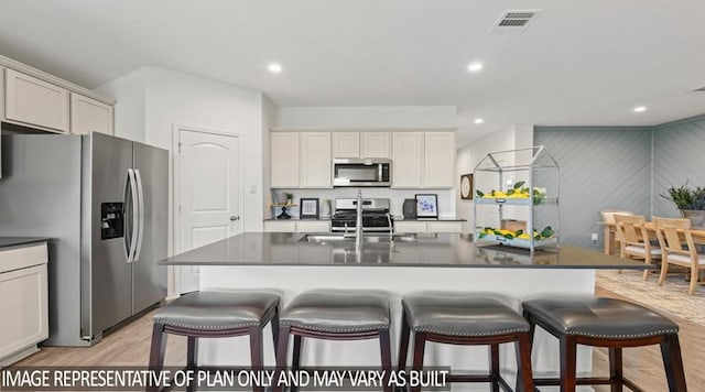 kitchen with a sink, dark countertops, a breakfast bar, light wood-style floors, and stainless steel appliances