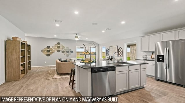 kitchen featuring a sink, ceiling fan, a center island with sink, dark countertops, and appliances with stainless steel finishes