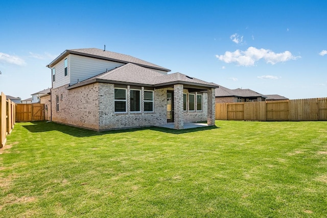 back of house featuring a fenced backyard, roof with shingles, a patio area, a lawn, and brick siding