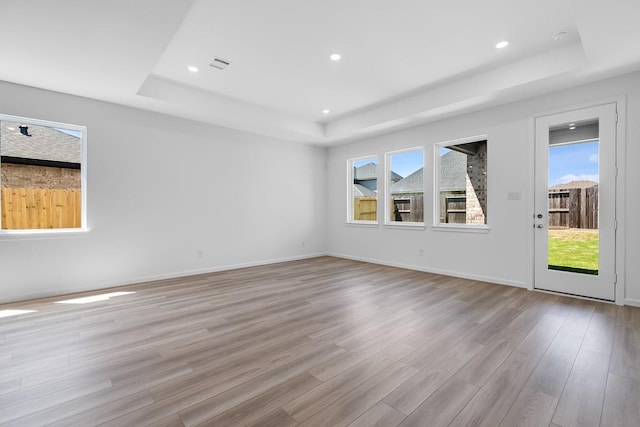 spare room with recessed lighting, a raised ceiling, and light wood-style flooring