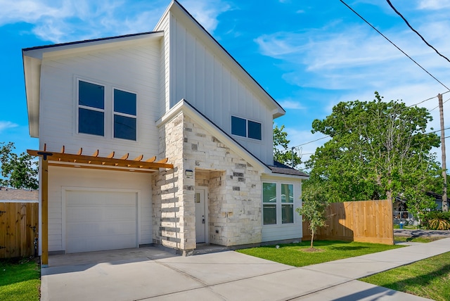 modern home with board and batten siding, driveway, fence, an attached garage, and stone siding