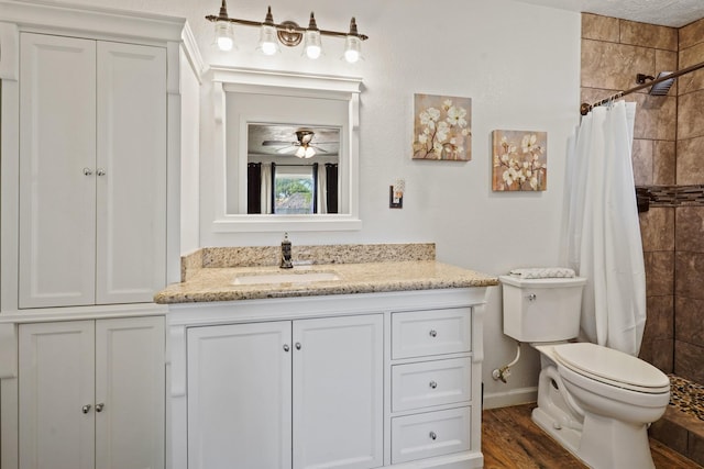 bathroom with toilet, a tile shower, a ceiling fan, vanity, and wood finished floors