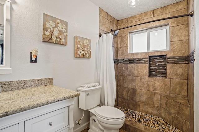 bathroom featuring vanity, baseboards, a stall shower, a textured ceiling, and toilet