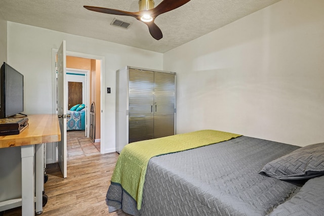 bedroom with light wood-style floors, a textured ceiling, a ceiling fan, visible vents, and baseboards