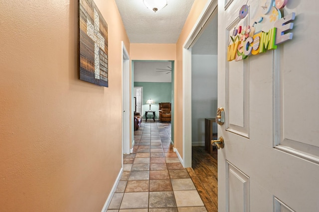 hall with baseboards, stone finish floor, and a textured ceiling