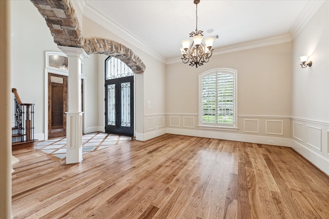 foyer with crown molding, arched walkways, an inviting chandelier, light wood finished floors, and ornate columns