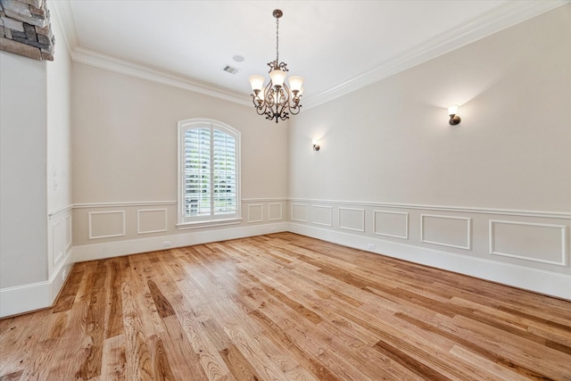 empty room featuring a notable chandelier, crown molding, a wainscoted wall, visible vents, and wood finished floors