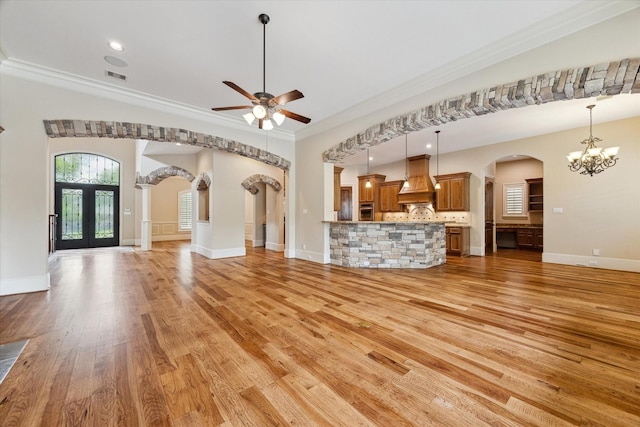 unfurnished living room with arched walkways, ornamental molding, and light wood finished floors