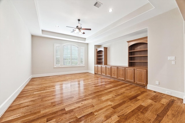 unfurnished living room featuring visible vents, a raised ceiling, a ceiling fan, and light wood-style floors