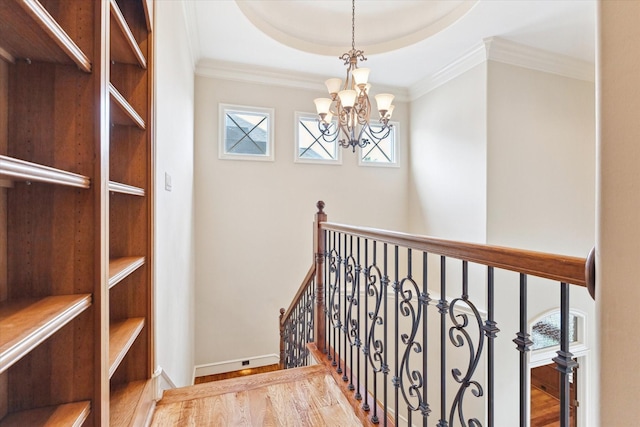 stairway with a tray ceiling, baseboards, an inviting chandelier, ornamental molding, and wood finished floors