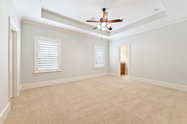 spare room featuring light colored carpet, a tray ceiling, baseboards, ornamental molding, and a ceiling fan