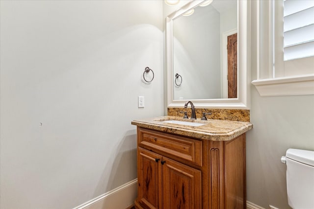 half bath featuring baseboards, toilet, and vanity