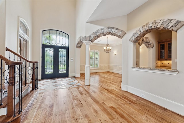 foyer with an inviting chandelier, light wood-type flooring, ornate columns, ornamental molding, and french doors