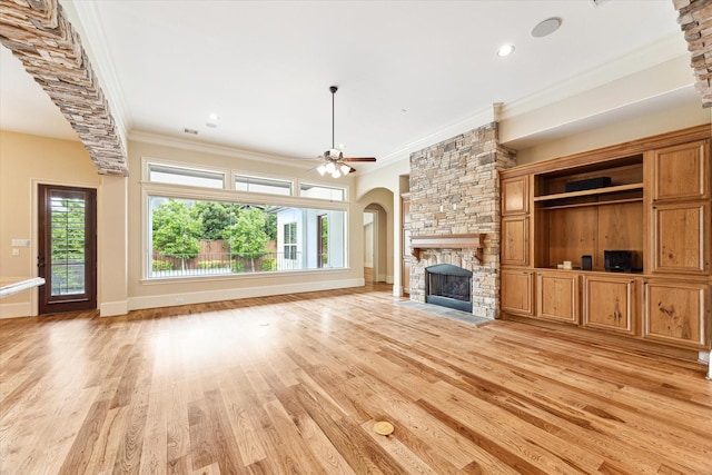 unfurnished living room with ornamental molding, arched walkways, light wood-style flooring, and a fireplace
