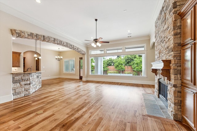 unfurnished living room with crown molding, ceiling fan with notable chandelier, a healthy amount of sunlight, and a fireplace