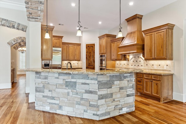 kitchen with brown cabinetry, light wood finished floors, and light stone counters