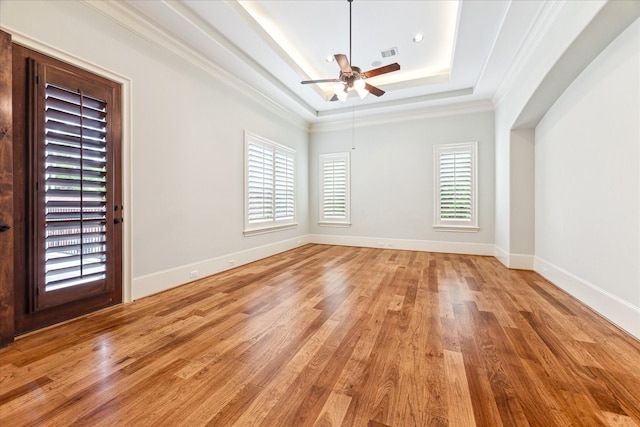 empty room with crown molding, visible vents, light wood-style floors, ceiling fan, and a tray ceiling