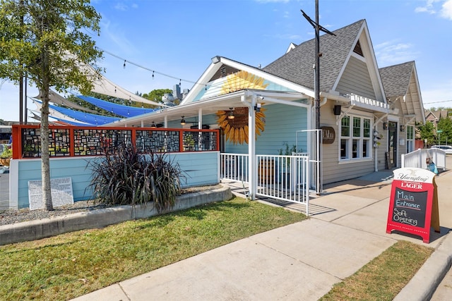 view of front of house featuring a porch, ceiling fan, a shingled roof, and a front lawn