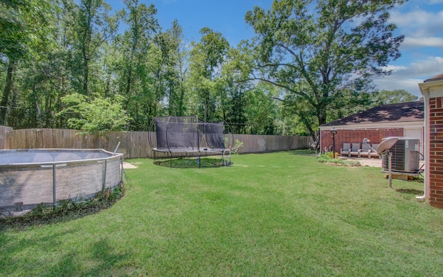 view of yard with central air condition unit, a fenced in pool, a trampoline, and a fenced backyard