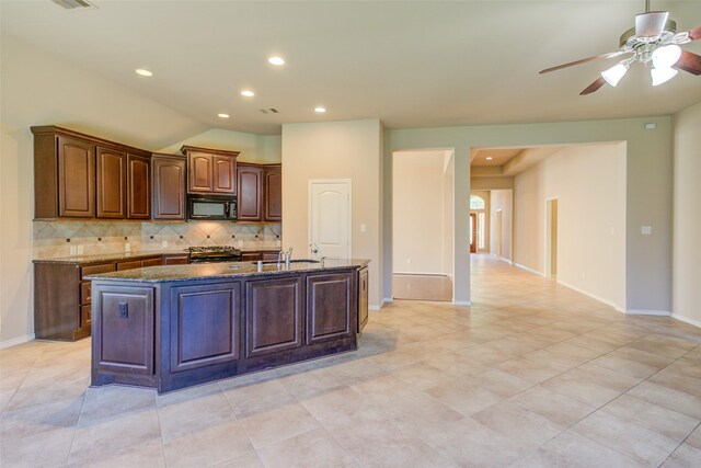 16007 Angler Bend Dr, Houston, TX 77044 - kitchen with black microwave, dark stone counters, a center island with sink, backsplash, and range