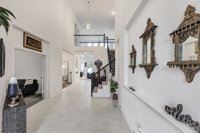 hallway with stairs, light tile patterned floors, and a towering ceiling