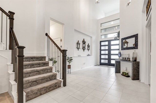 foyer featuring visible vents, baseboards, a high ceiling, stairway, and light tile patterned flooring