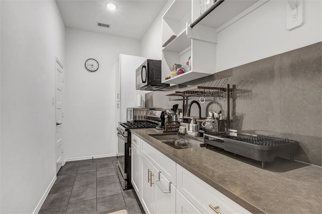 kitchen with black microwave, visible vents, gas range, a sink, and dark countertops