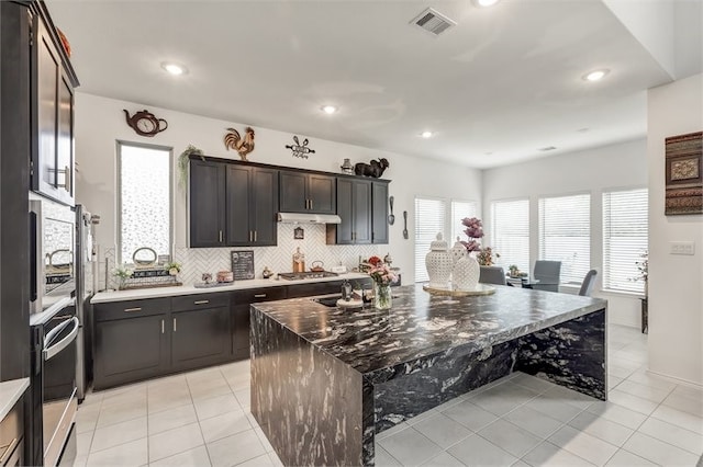kitchen with tasteful backsplash, visible vents, appliances with stainless steel finishes, under cabinet range hood, and light tile patterned flooring
