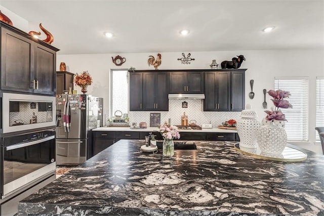 kitchen with stainless steel appliances, under cabinet range hood, backsplash, and dark brown cabinets
