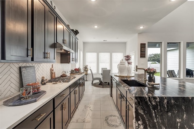 kitchen with tasteful backsplash, dark stone countertops, a kitchen island with sink, stainless steel gas stovetop, and a sink