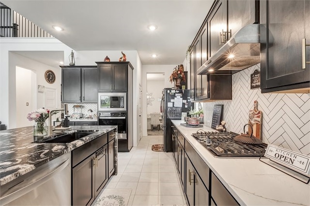 kitchen featuring light tile patterned floors, light stone countertops, extractor fan, appliances with stainless steel finishes, and a sink