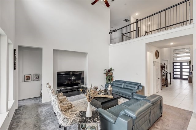 carpeted living area featuring tile patterned floors, a towering ceiling, visible vents, and ceiling fan