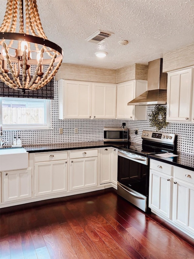 16111 Queensdale Dr, Houston, TX 77082 - kitchen featuring wall chimney range hood, white cabinets, dark countertops, appliances with stainless steel finishes, and visible vents