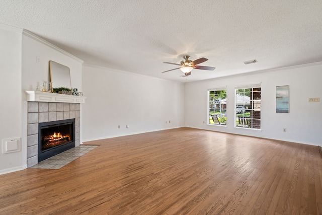 unfurnished living room with a tiled fireplace, ceiling fan, visible vents, a textured ceiling, and wood finished floors