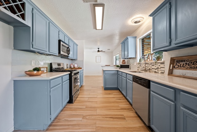 kitchen with blue cabinets, appliances with stainless steel finishes, light wood-style flooring, and a sink