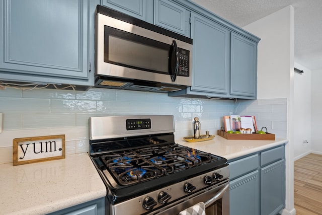 kitchen with blue cabinets, stainless steel appliances, backsplash, light wood finished floors, and baseboards