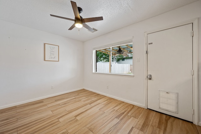 spare room with a textured ceiling, ceiling fan, visible vents, baseboards, and wood finished floors