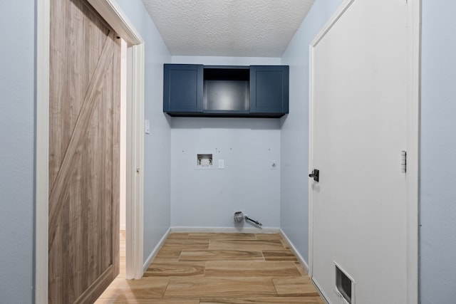 washroom featuring hookup for a washing machine, cabinet space, light wood-type flooring, visible vents, and a textured ceiling