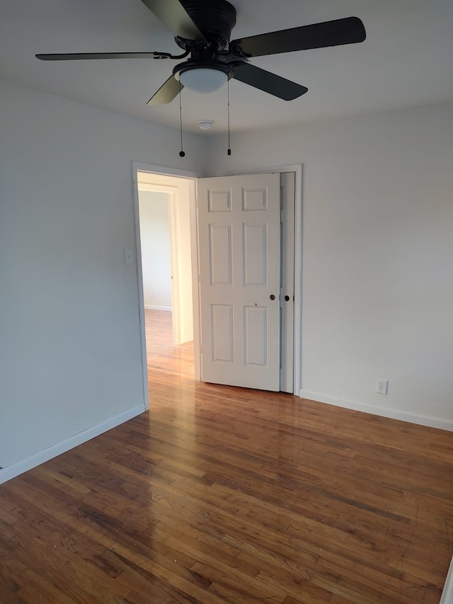 empty room featuring wood finished floors, baseboards, and a ceiling fan