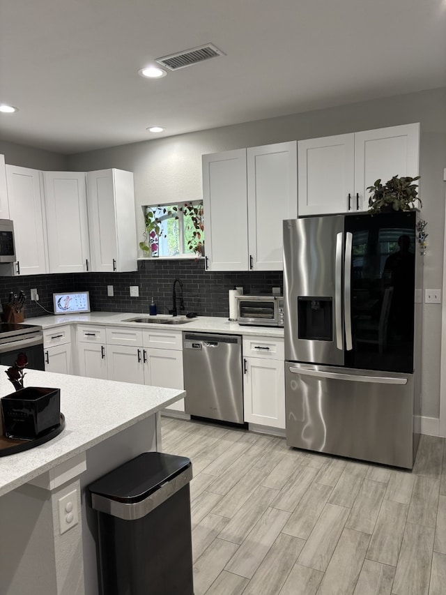15888 Chestnut Dr, Montgomery, TX 77356 - kitchen featuring white cabinetry, visible vents, appliances with stainless steel finishes, a sink, and backsplash