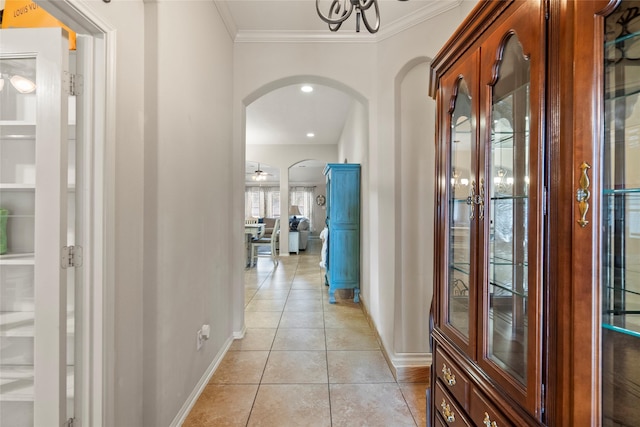 hall with arched walkways, baseboards, crown molding, and light tile patterned flooring