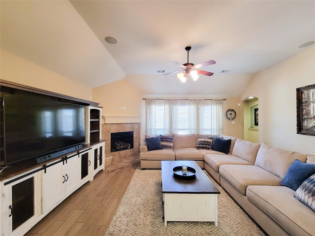living area with a fireplace, a ceiling fan, visible vents, lofted ceiling, and light wood finished floors