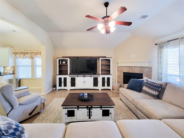 living area featuring visible vents, lofted ceiling, arched walkways, a tile fireplace, and ceiling fan