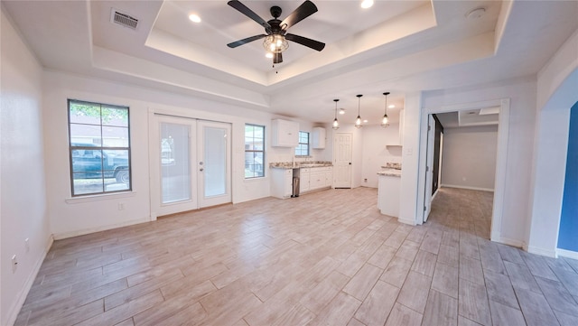 interior space featuring white cabinets, light wood finished floors, visible vents, and a tray ceiling